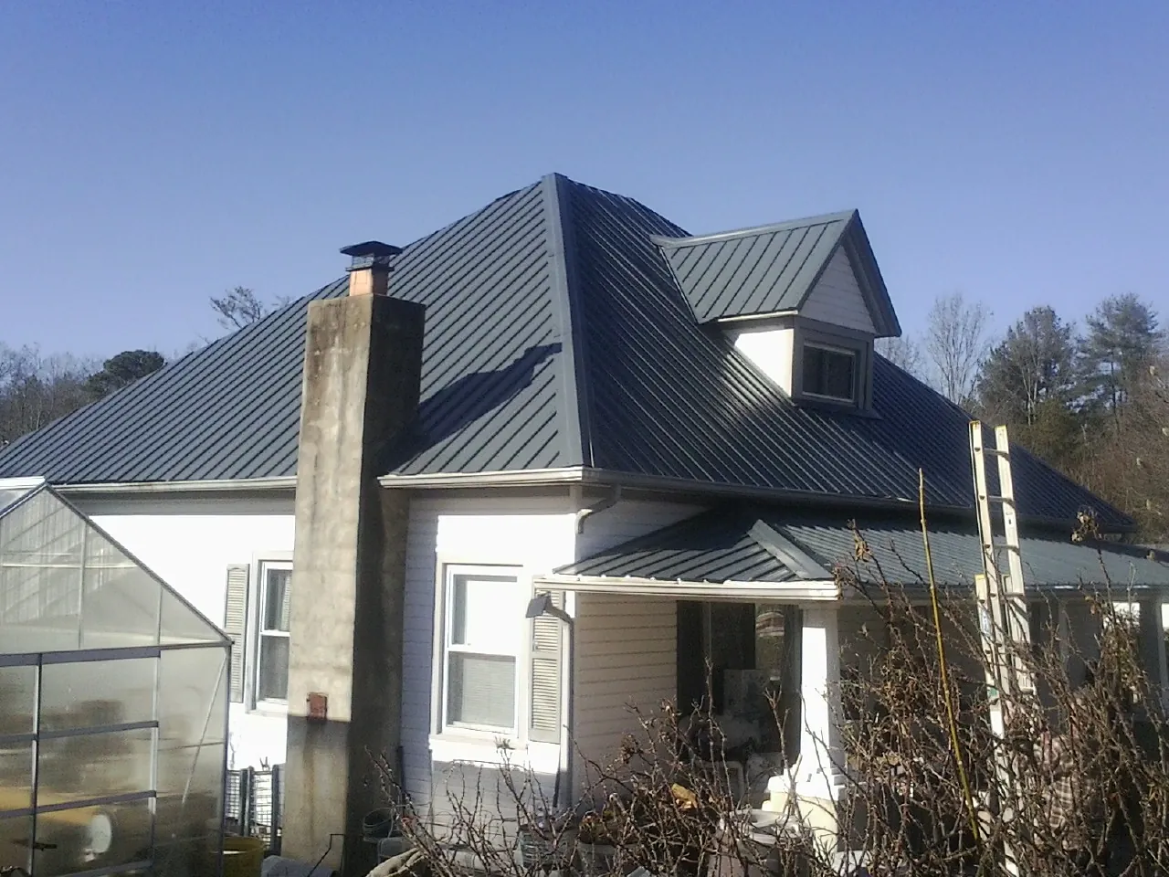 Dark blue standing seam metal roof on a white farmhouse with dormer — Slate & Tile Roof Repair by Roofing Brothers in Snellville