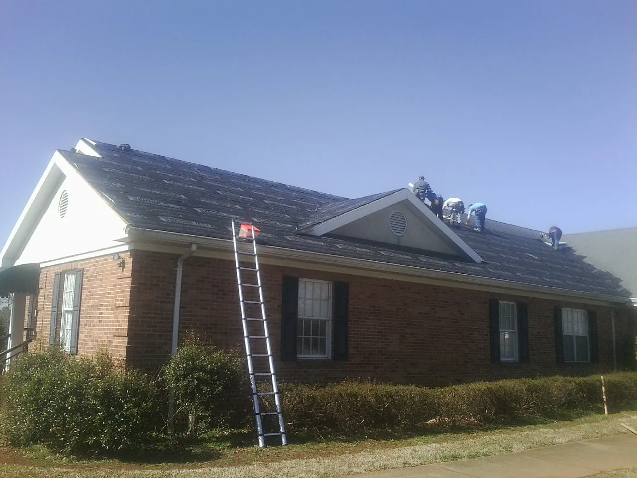 Crew tearing shingles off a brick ranch roof with a ladder set — Emergency Roof Repair work by our crew in Snellville