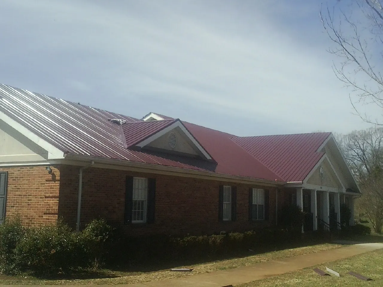 Red metal roof with gabled entries on a long brick building, from a Hail Damage Roof Repair job in Snellville