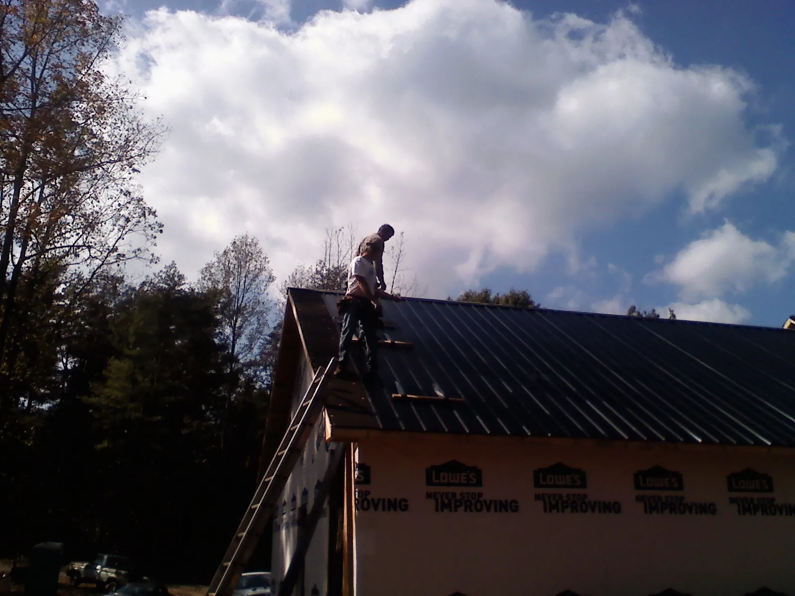 Roofer fastening dark metal panels high against a cloudy sky, from a Roof Inspection job in Snellville