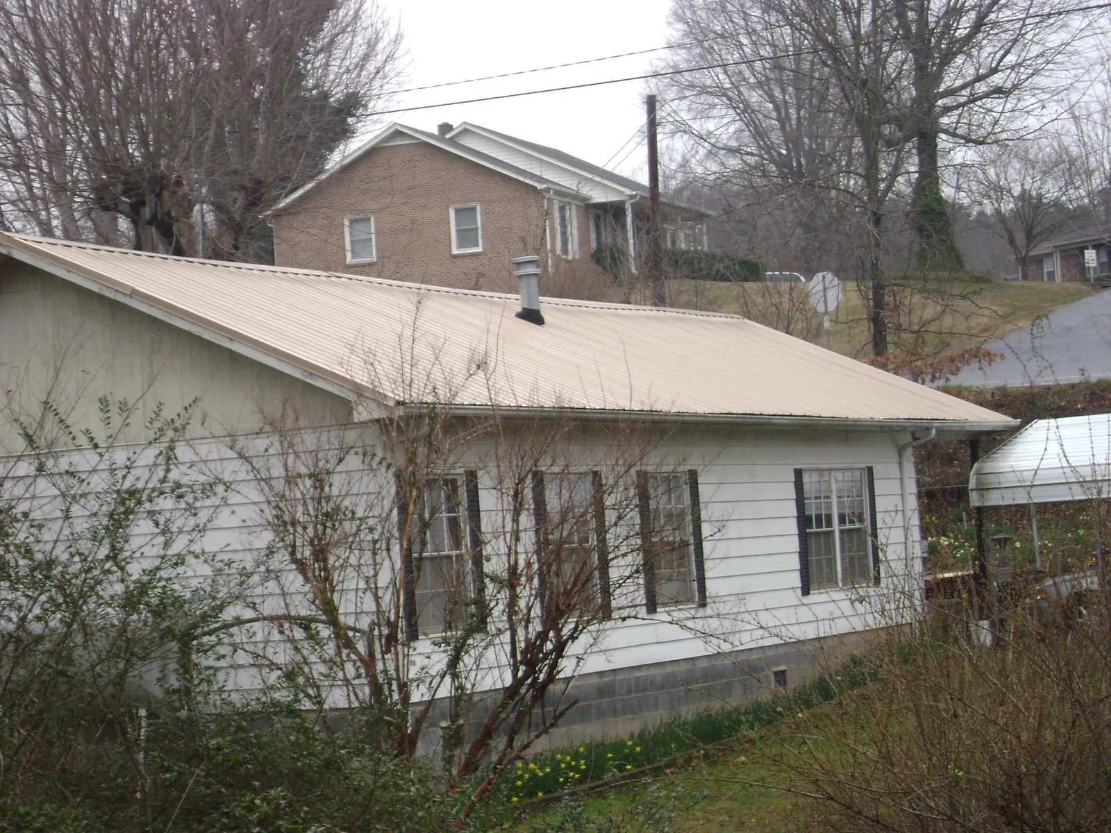Tan metal roof on a white sided house set into a hillside — Commercial Roofing by Roofing Brothers in Snellville